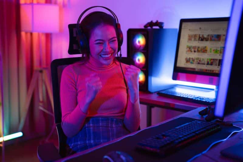 Jogadora comemora vitória na partida usando alguns acessórios para setup gamer essenciais ao alto desempenho.