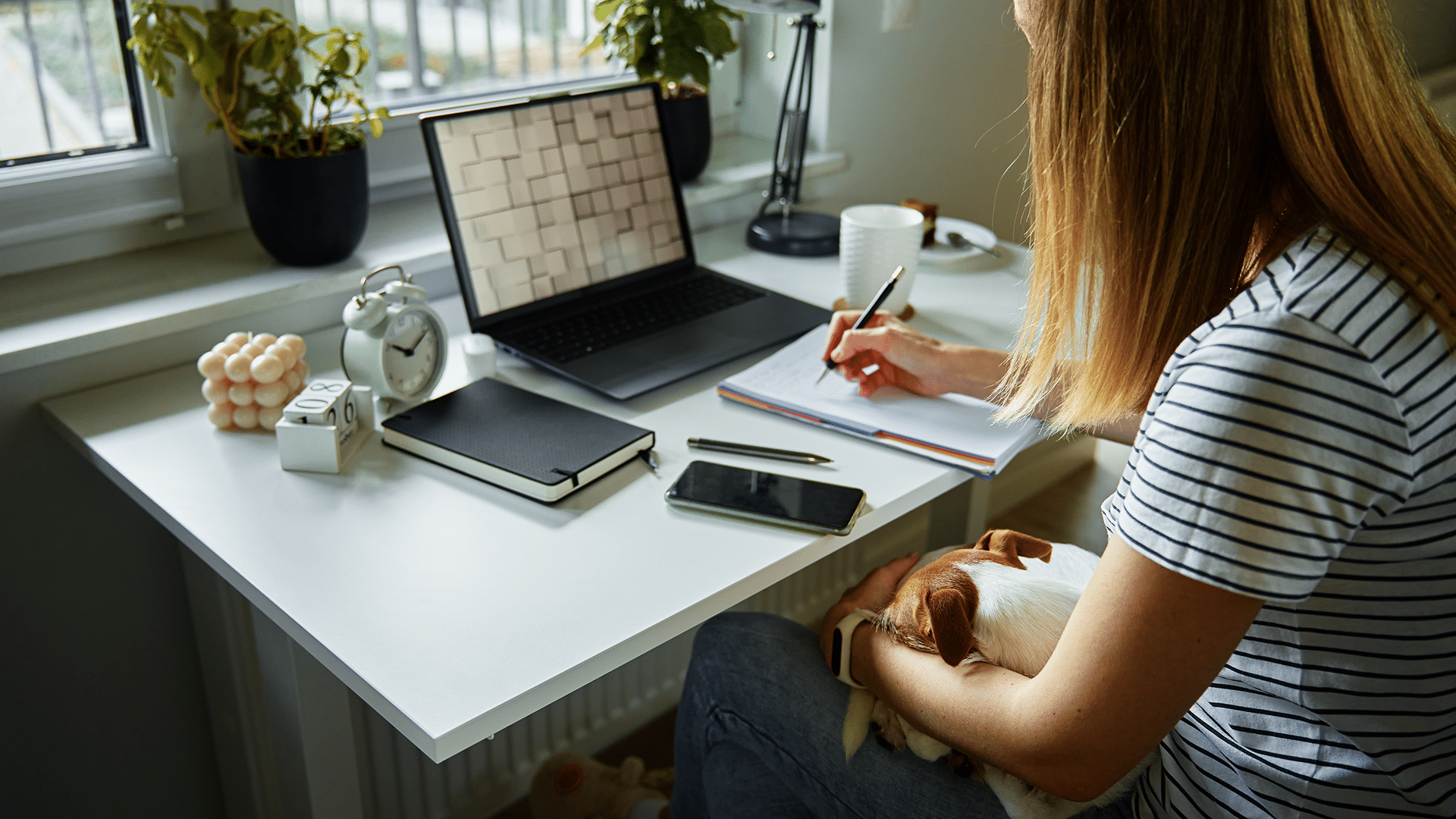 mulher de costas sentada em uma cadeira de escritório em uma mesa branco com um notebook em sua frente e outros itens de homo office